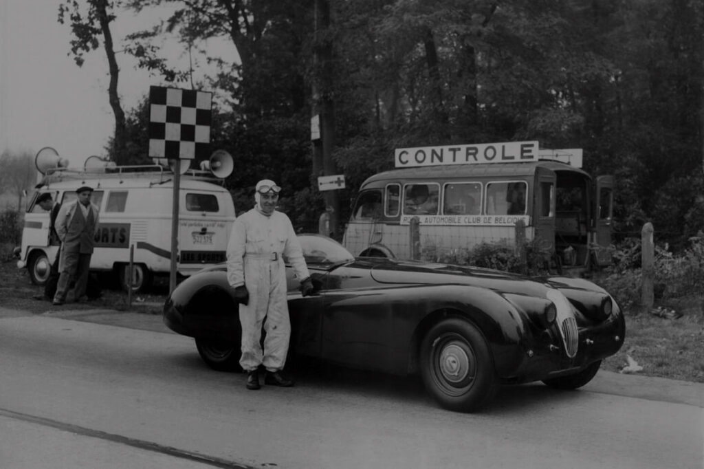 Man standing next to vintage jaguar car with two vehicles in background