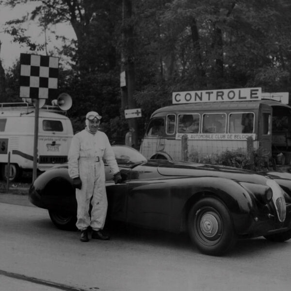 Man standing next to vintage jaguar car with two vehicles in background