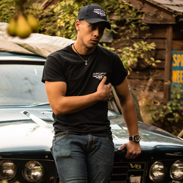 Man wearing zero west cap and t-shirt leaning on a car