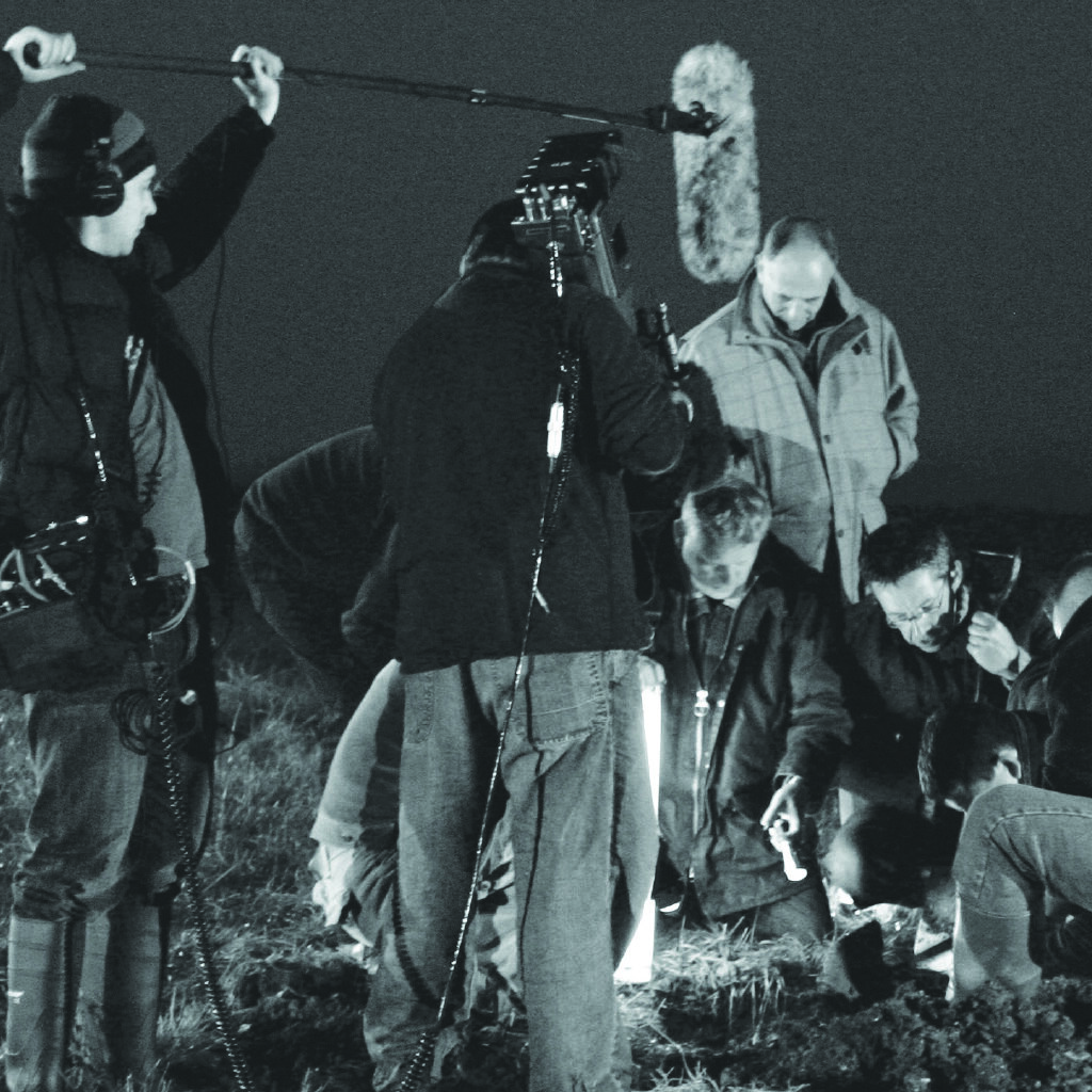 Two men filming a group of men digging up pieces of Lancaster bomber ED825