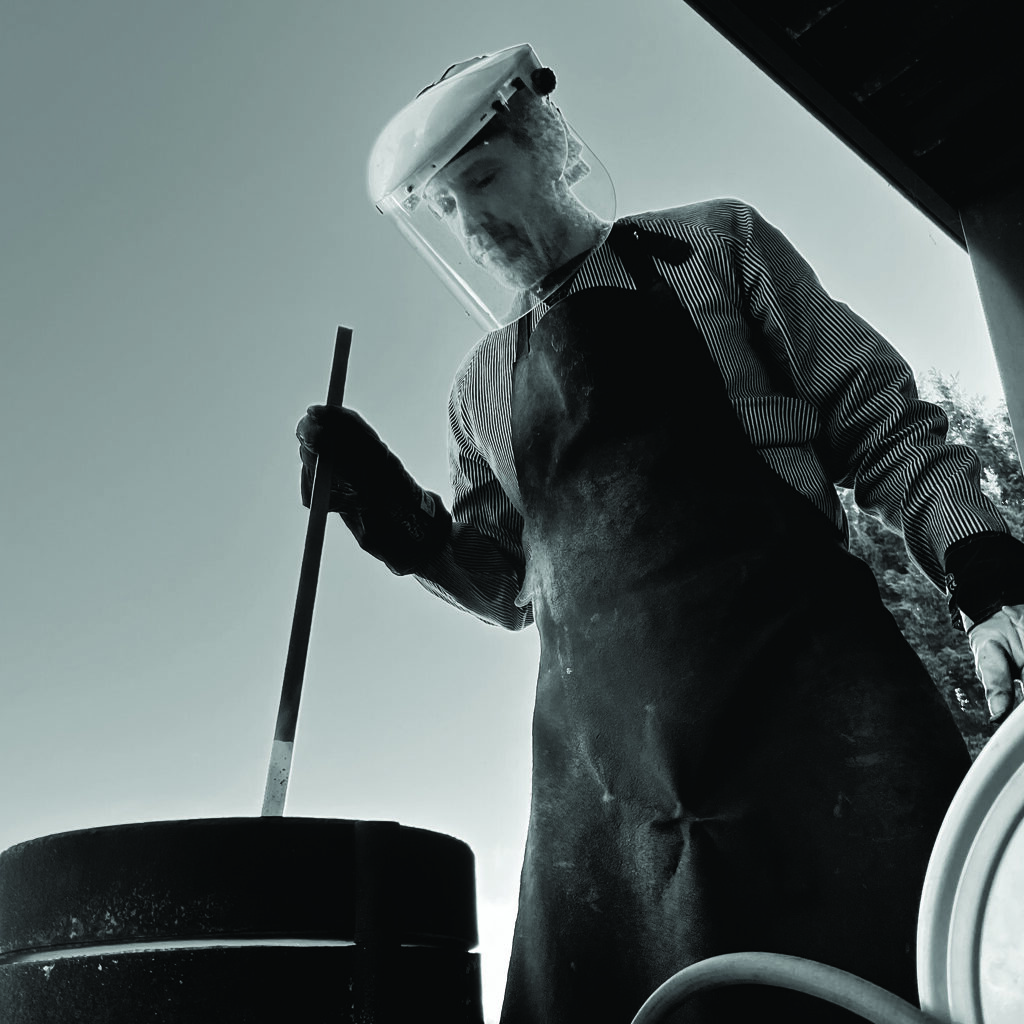 Man wearing a visor stirring Lancaster metal in a furnace