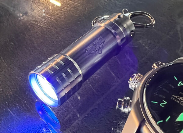 Zero West mini Ultraviolet Torch on metal table with watch
