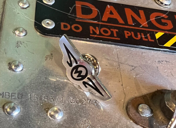 Zero West Pin badge on metal table with danger sign
