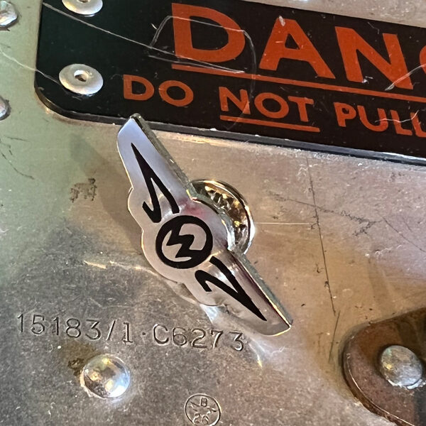 Zero West Pin badge on metal table with danger sign